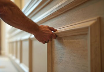 Close-up of traditional wooden panelled wall with raised framing, showing hand positioning final piece